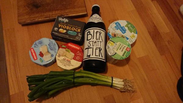 obazda einkauf: margarine, zwei weich"käse", ein bier, vegane streichcreme, ein bund frühlingszwiebeln auf einem holztisch